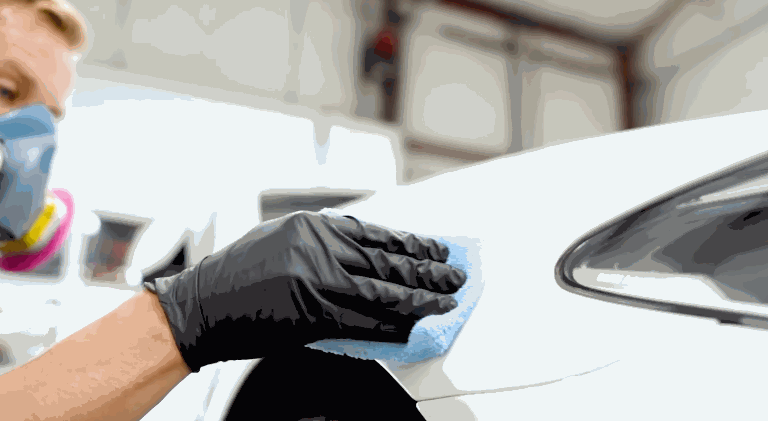A gloved technician preps the surface of a white car panel with a blue cloth before applying paint protection film.