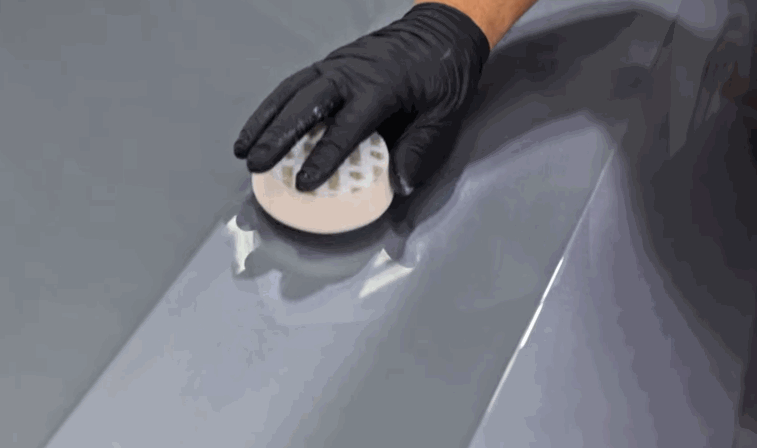 A dual-action polisher is used with a white pad to refine a coated gray panel, ensuring a smooth and high-gloss finish.