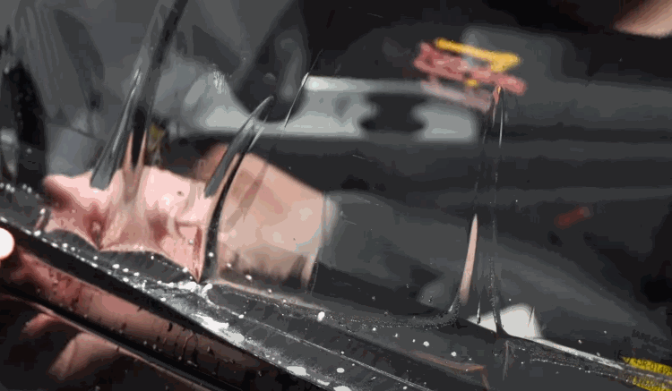 A person aligns and presses clear tint film onto a side car window, ensuring it fits snugly along the edges.