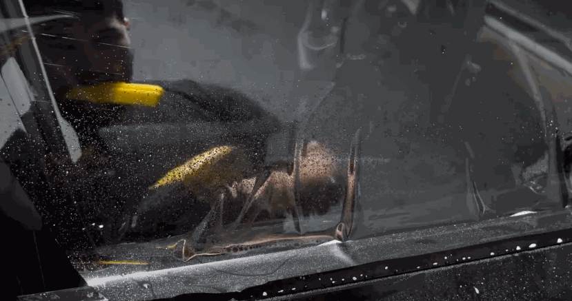 A technician smooths tint film across a rear car window with a yellow squeegee tool, pushing out water and air.